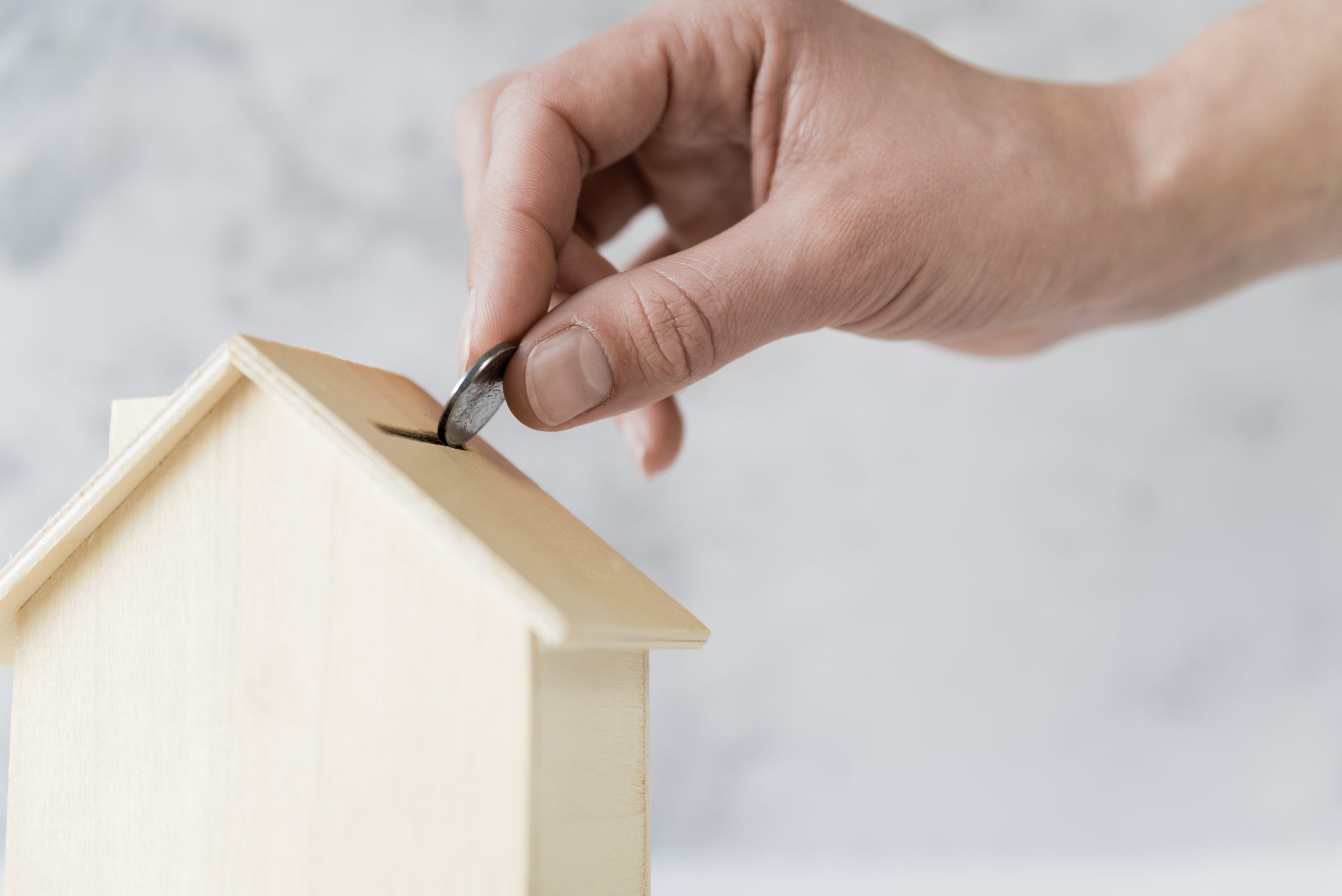 primer-plano-mano-persona-insertando-moneda-alcancia-casa-madera