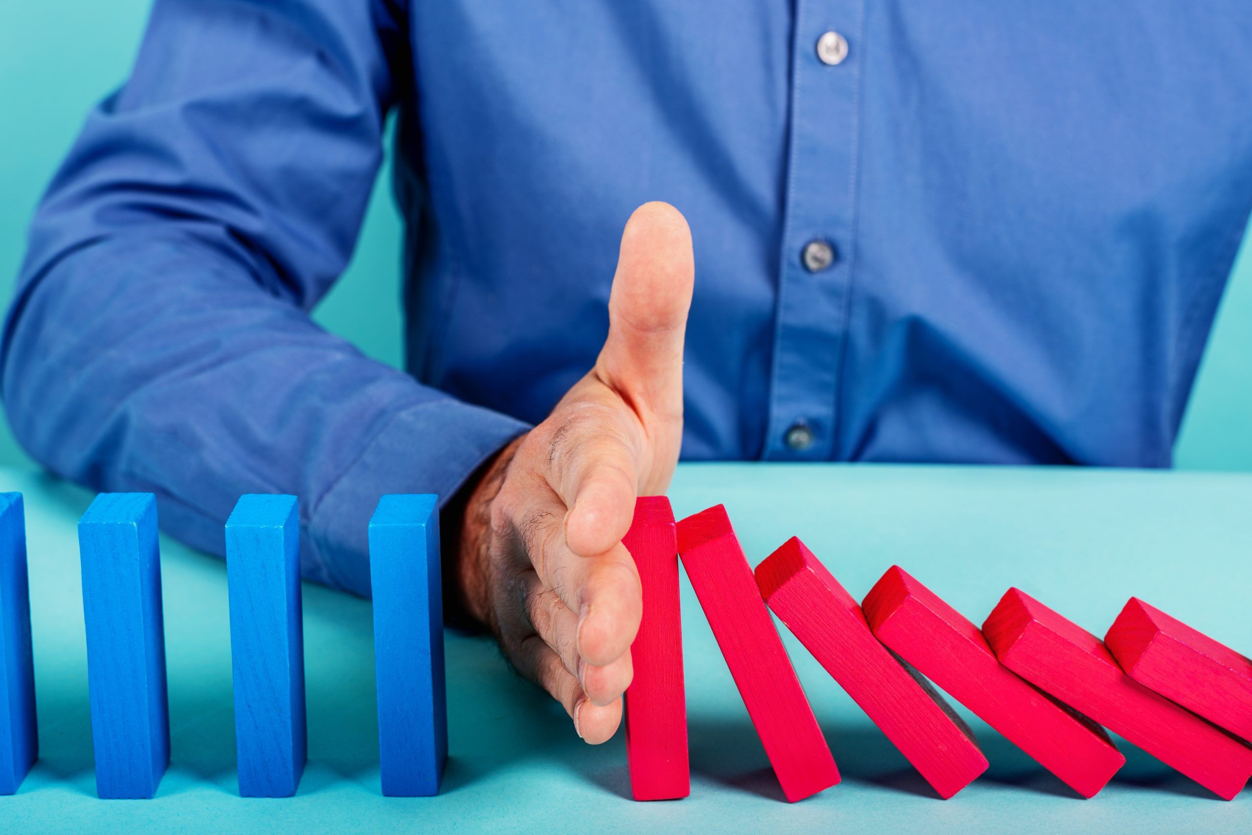 Businessman stops a chain fall like domino game. Concept of preventing crisis and failure in business.